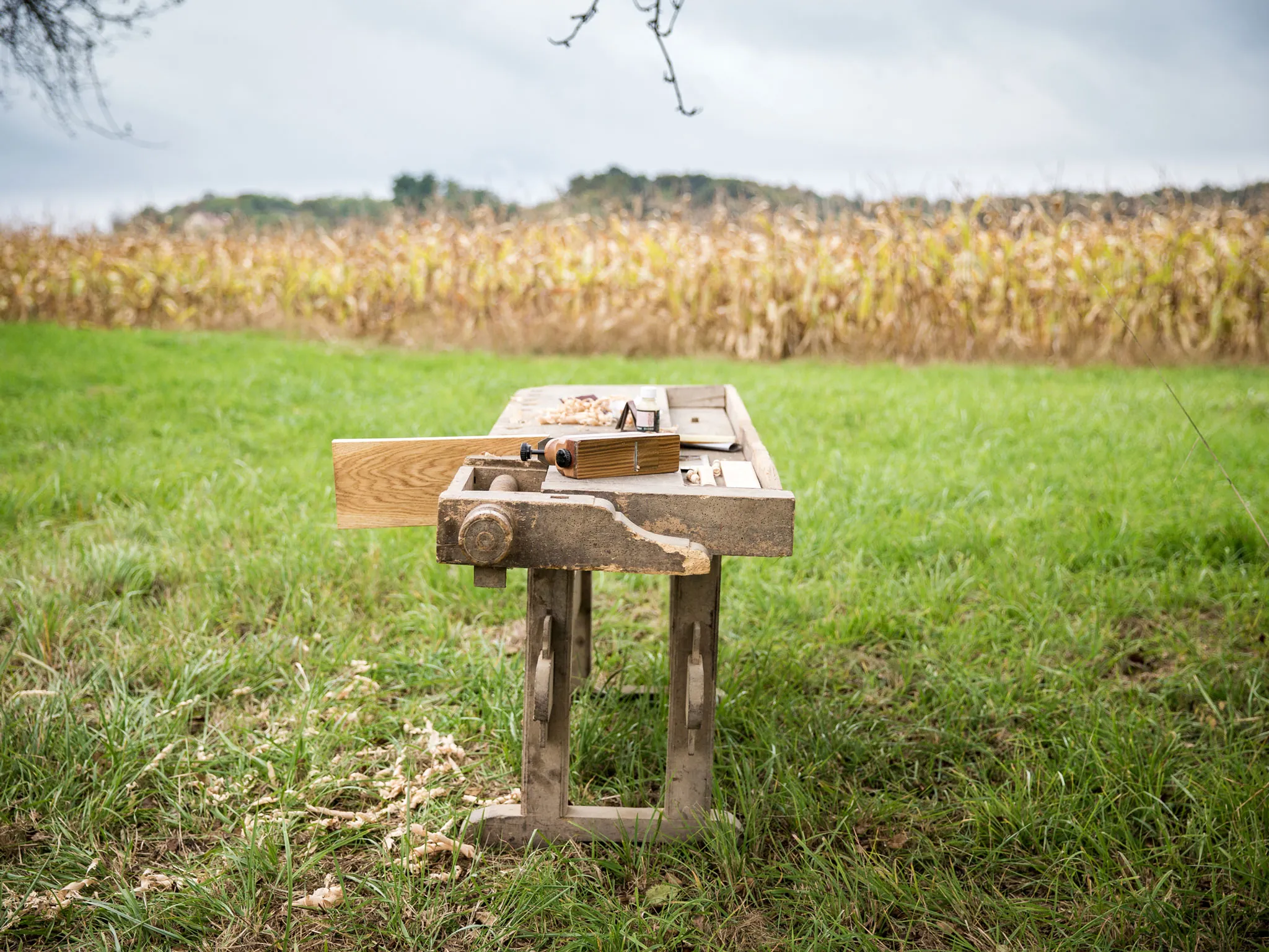 Alte Hobelbank mit Handwerkzeug auf einer Wiese vor einem Feld